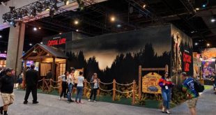 Attendees at New York Comic Con walk past a large Peacock Camp Crystal Lake booth featuring a dark forest mural and a wooden sign.